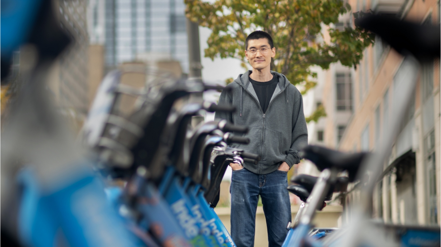 Xiaoxia Dong standing with hands in pockets next to rack of Indego rental bicycles in Philadelphia