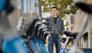 Xiaoxia Dong standing with hands in pockets next to rack of Indego rental bicycles in Philadelphia