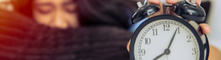 A teenager lays down and reaches for an alarm clock after having trouble sleeping.