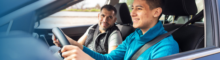 Teen boy driving smiling looking at the road while dad smiles in the passenger seat