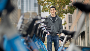 Xiaoxia Dong standing with hands in pockets next to rack of Indego rental bicycles in Philadelphia