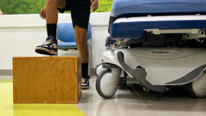 A young child steps up with his right foot onto a wooden box as part of a step test exam during concussion treatment.