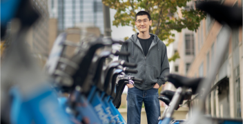 Xiaoxia Dong standing with hands in pockets next to rack of Indego rental bicycles in Philadelphia