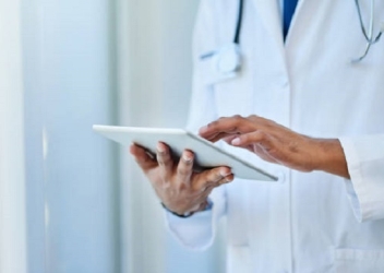A doctor checks items off a digital health record while using a tablet device.