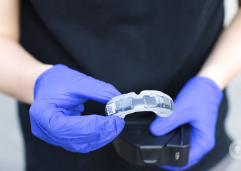 A medical professional holds a smart mouthguard in their hands while wearing sterile gloves.
