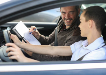 Teen boy driver talking to smiling male driving instructor holding clipboard