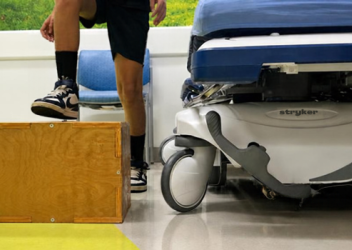 A young child steps up onto a wooden box as part of a modified step test being conducted inside a clinical room at the CHOP King of Prussia hospital.